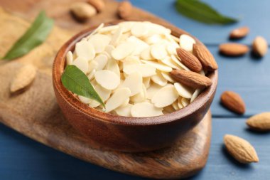 Taze badem taneleri, bütün fındıklar ve yeşil yapraklar mavi ahşap masada, yakın plan.