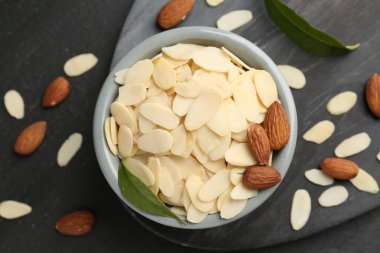 Fresh almond flakes, whole nuts and green leaves on grey table, flat lay