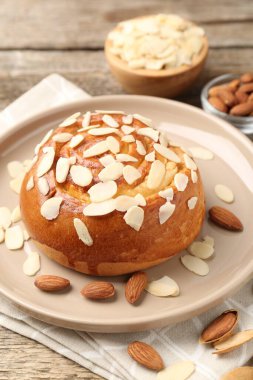 Tasty roll bun with almond flakes and nuts on wooden table, closeup