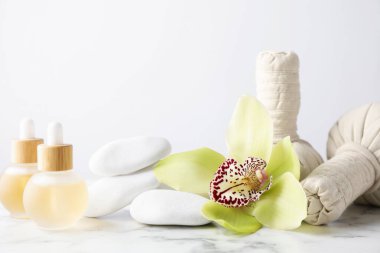 Beautiful spa composition with essential oils and herbal bags on white marble table against light background, closeup