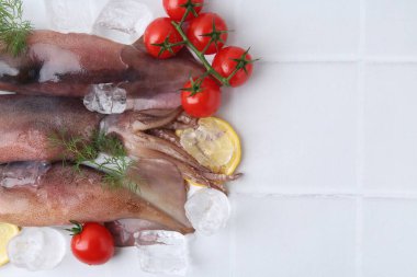 Raw squids, ice cubes, tomatoes, lemon slices and dill on white tiled table, flat lay. Space for text