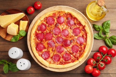 Lezzetli pepperoni pizza ve malzemeler ahşap masada, düz yerde.