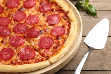 Lezzetli kesilmiş pepperoni pizza, servis ve ahşap masada taze fesleğen, yakın plan.