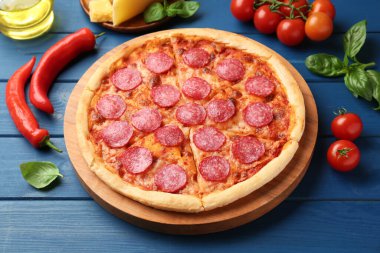 Lezzetli biberli pizza ve mavi ahşap masada malzemeler.