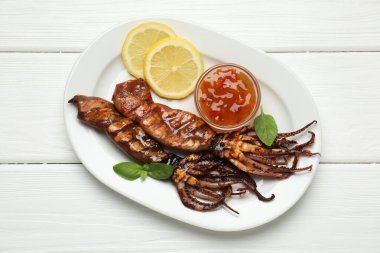 Beyaz ahşap masada limon, sos ve fesleğenle servis edilen lezzetli kalamar.