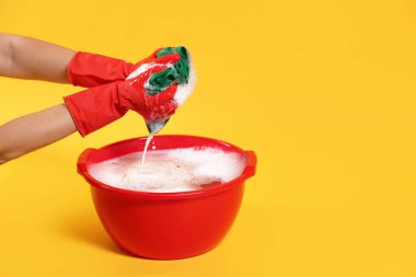 Sarı arka planda plastik leğende çamaşır yıkayan kadın, yakın plan. Metin için boşluk