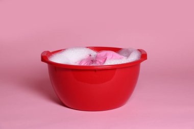 Pembe arka planda giysi, su ve köpüklü plastik leğen.