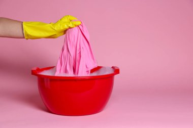 Kadın elbiselerini pembe arka planda plastik bir leğende yıkıyor, yakın plan. Metin için boşluk