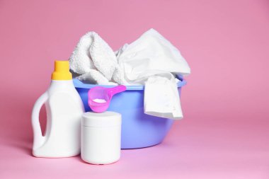 Çamaşırları ve pembe arka planda deterjanları olan plastik bir leğen. Metin için boşluk