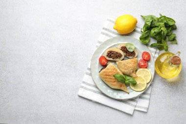 Pieces of tasty grilled squid stuffed with mushrooms, basil, tomatoes and lemon on light grey textured table, flat lay. Space for text