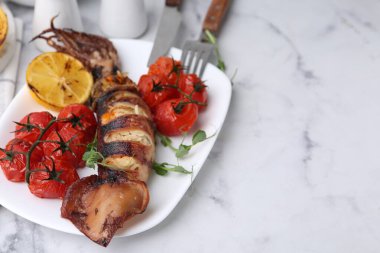 Tasty stuffed squid, microgreens, lemon and tomatoes on white marble table, closeup. Space for text