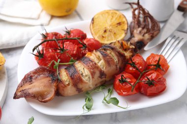 Tasty stuffed squid, microgreens, lemon and tomatoes on white marble table, closeup