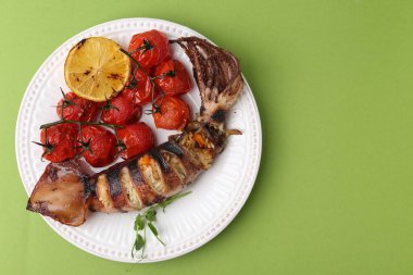 Tasty stuffed squid, microgreens, lemon and tomatoes on green background, top view. Space for text