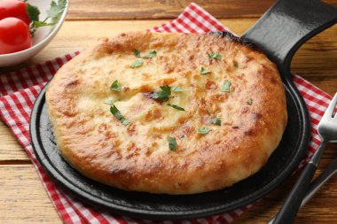 Delicious Megrelian khachapuri with parsley served on wooden table, closeup