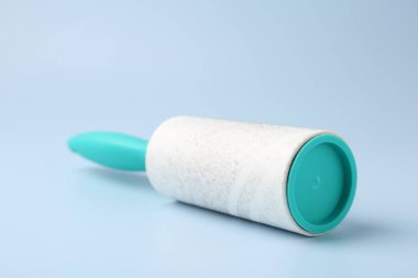 Lint roller with used sticky tape on light blue background, closeup