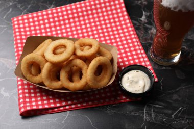 Siyah mermer masada servis edilen soslu ve biralı kızarmış kalamar halkaları, yakın plan.