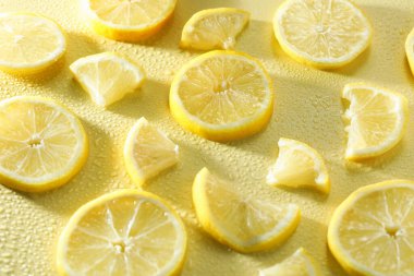 Sarı arka planda limon ve su damlaları, yakın plan.