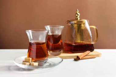 Cam bardaklarda lezzetli Türk çayı, çaydanlık, esmer şeker ve tarçın beyaz mermer masa üzerinde renk arka planına karşı, yakın plan