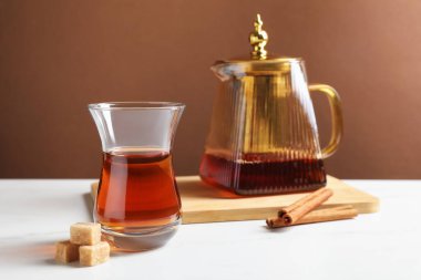 Cam fincanda lezzetli Türk çayı, çaydanlık, esmer şeker ve tarçın beyaz mermer masa üzerinde renk arka planına karşı, yakın plan