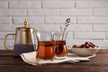 Cam bardaklarda lezzetli Türk çayı, beyaz tuğla duvara karşı ahşap masada hurma ve çaydanlık.