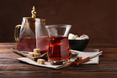 Cam bardakta lezzetli Türk çayı, kahverengi şeker, tarçın, tatlı ve çaydanlık ahşap masada renk arka planına karşı, yakın plan