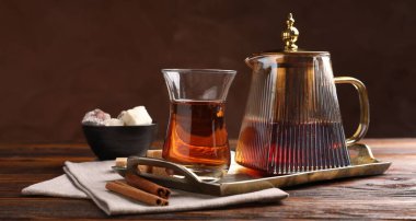 Cam bardakta lezzetli Türk çayı, kahverengi şeker, tarçın, tatlı ve çaydanlık ahşap masada renk arka planına karşı, yakın plan