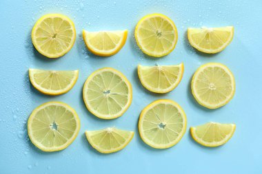 Limon dilimleri ve su damlaları açık mavi arkaplanda, düz yerde.