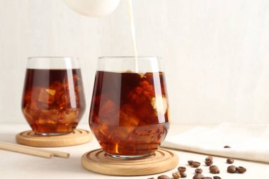 Beyaz masada buzlu kahve bardağına süt dökerek.