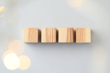 Blank wooden cubes on light grey background, flat lay. Bokeh effect