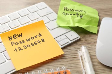 Şifre değiştiriliyor. Yeni ve eski şifreli kâğıt notalar, ahşap masa üzerinde kırtasiye ve klavye, yakın plan