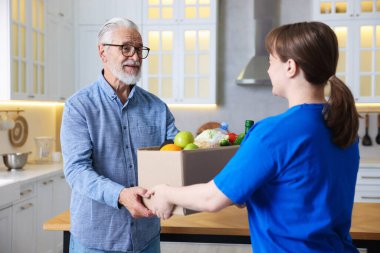 Yaşlılar için insani yardım. Gönüllü, içinde yiyecek olan karton kutuları evin içindeki yaşlı adama veriyor.