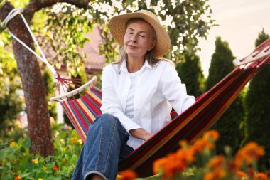 Hamakta dinlenen hasır şapkalı yaşlı kadın.