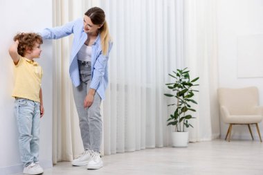 Anne, küçük kızının boyunu içeride beyaz duvarın yanında ölçüyor. Metin için boşluk