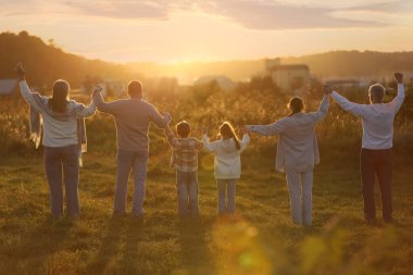 Aile kucaklaşması ve yükselen eller gün batımında, arka manzara