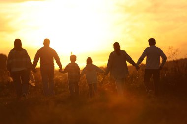 Aile gün batımında, arka planda el ele tutuşuyor.