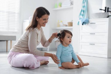 Anne banyoda bebeğinin saçını tarıyor.