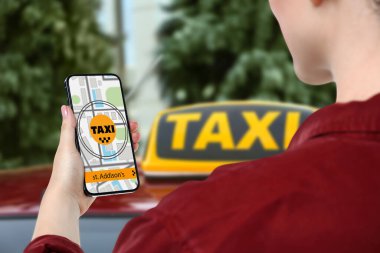 Şehir caddesinde taksi çağırmak için cep telefonu uygulaması kullanan bir kadın.