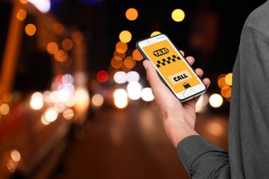 Adam cep telefonundaki uygulamayı kullanarak gece şehir caddesinde taksi çağırıyor.