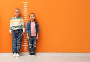 Turuncu duvarın yanında ölçekli kardeşler ya da arkadaşlar. Yükseklik ölçümü