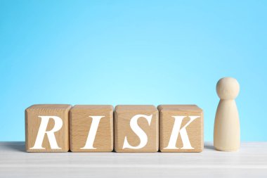 Açık mavi arka plana karşı beyaz masadaki tahta küpler ve insan figüründen yapılmış risk sözcükleri