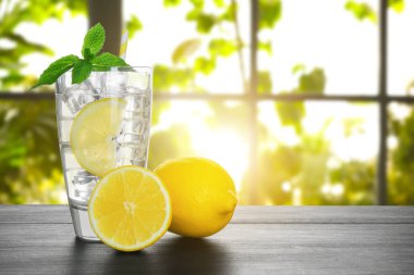 Lemon water and ice cubes in glass on wooden table against window indoors