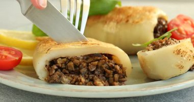 Gri desenli masada mantarla doldurulmuş lezzetli ızgara kalamar kesen kadın, yakın plan.