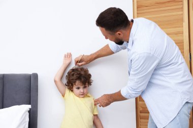 Baba, evdeki küçük oğlunun boyunu beyaz duvarın yanında ölçüyor. Metin için boşluk