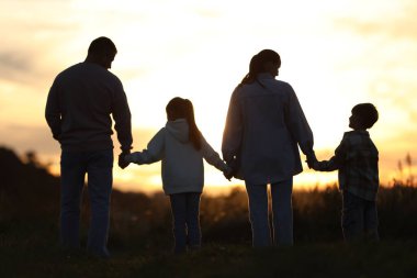 Aile gün batımında, arka planda el ele tutuşuyor.