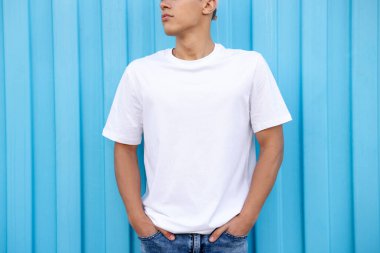 Açık mavi duvarın yanında beyaz tişört giyen genç adam, yakın plan. Tasarım için model