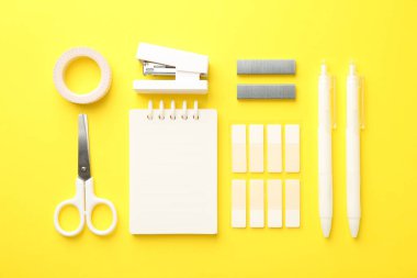 Stapler and other stationery on yellow background, flat lay