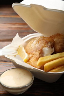 British Traditional Fish and chips with lemon and sauce on wooden table, closeup