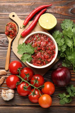Delicious salsa sauce in bowl and ingredients on wooden table, flat lay