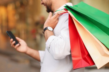 Farklı alışveriş çantaları ve açık havada telefonu olan adam, yakın plan.