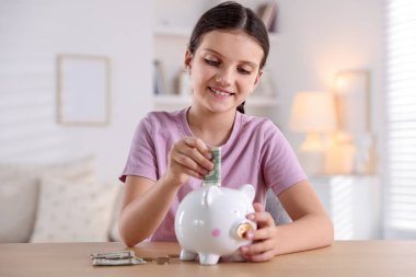 Gülümseyen küçük kız, kapalı alandaki ahşap masadaki kumbaralara para yatırıyor. Cep harçlığı ve sorumluluk